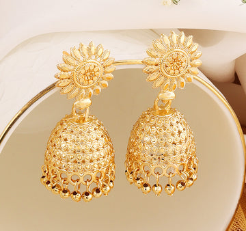 A pair of intricately designed gold-plated jhumka earrings from the Mekkna brand, featuring detailed craftsmanship and a luxurious finish.