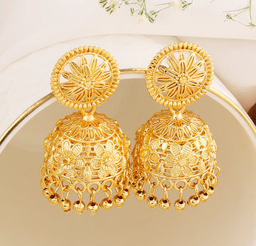 A pair of intricately designed gold-plated jhumka earrings from the Mekkna brand, featuring detailed craftsmanship and a luxurious finish.