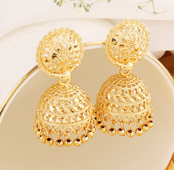 A pair of intricately designed gold-plated jhumka earrings from the Mekkna brand, featuring detailed craftsmanship and a luxurious finish.