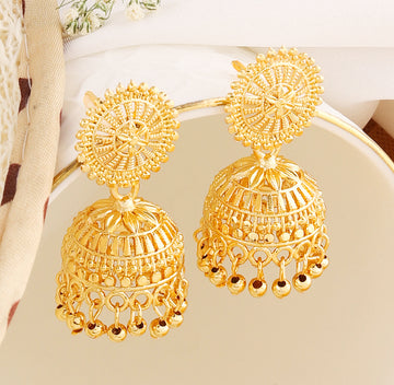 A pair of intricately designed gold-plated jhumka earrings from the Mekkna brand, featuring detailed craftsmanship and a luxurious finish.