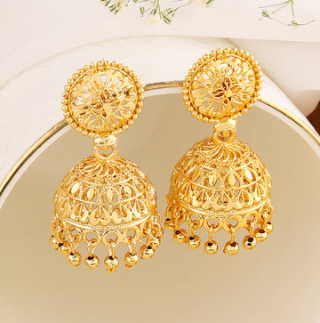 A pair of intricately designed gold-plated jhumka earrings from the Mekkna brand, featuring detailed craftsmanship and a luxurious finish.